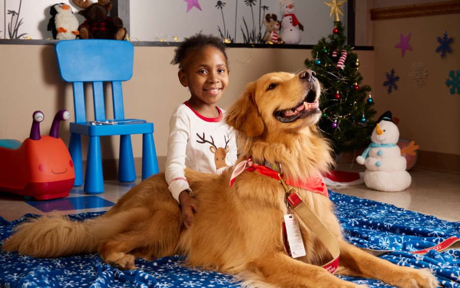 A patient smiles at the camera while posing with a therapy dog