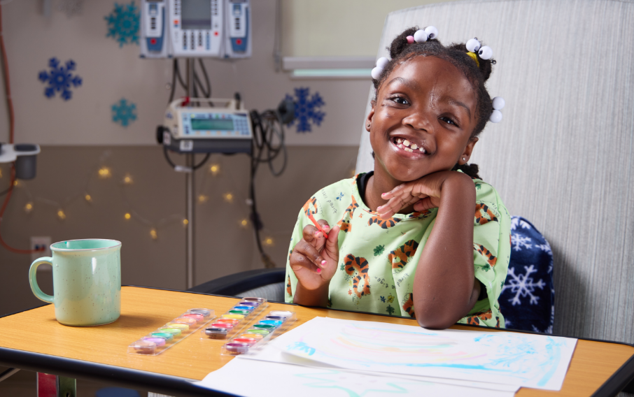 A young patient smiles at the camera while engaged in a watercolor painting activity