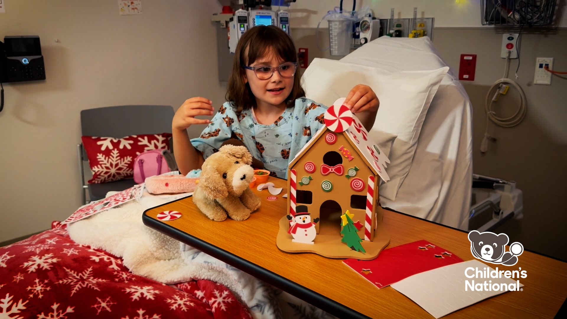 A young female patient sitting in a bed decorates a gingerbread house art project