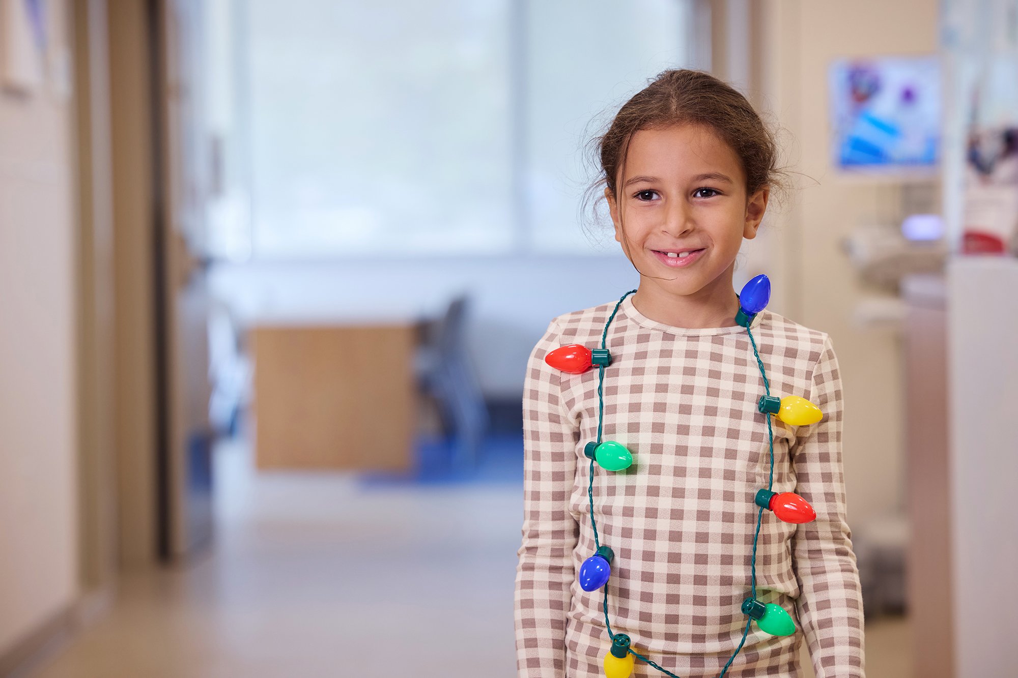 CNH patient Basma, age 7, smiles at the camera while wearing a holiday light necklace.