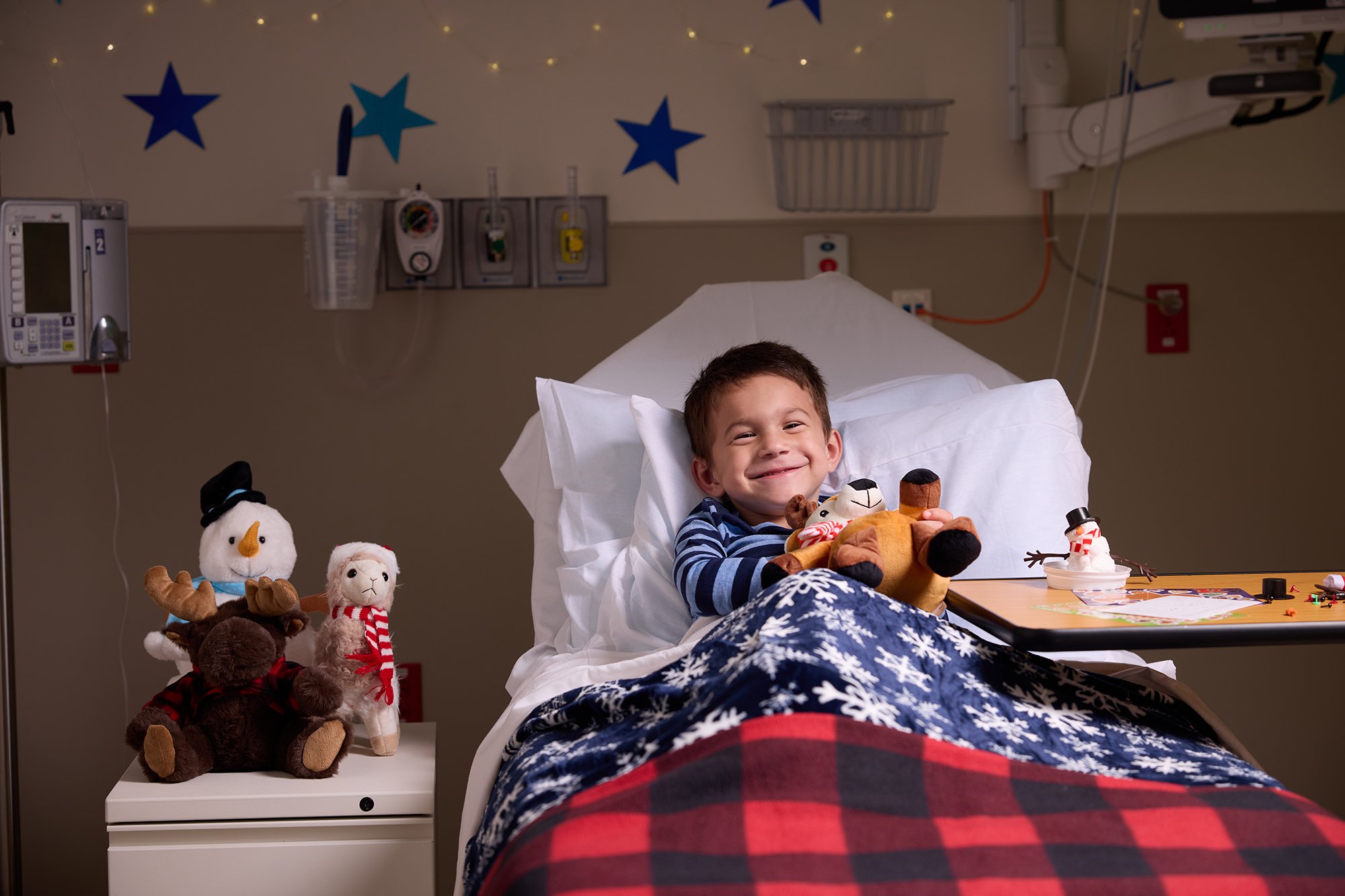 CNH patient Elliot, age 5, smiles at the camera while laying in a hospital bed and hugging a stuffed animal.