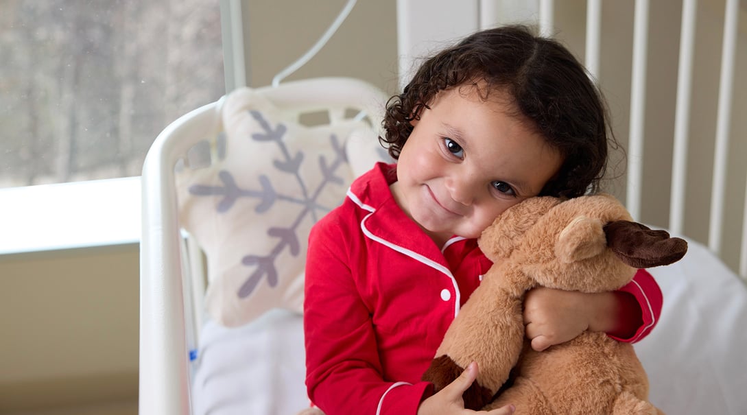 CNH patient, Emmylou, cuddles a stuffed reindeer toy while wearing red pajamas.