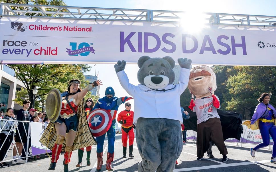 A jubilant scene at The Race for Every Child with Dr. Bear crossing the finish line alongside runners.