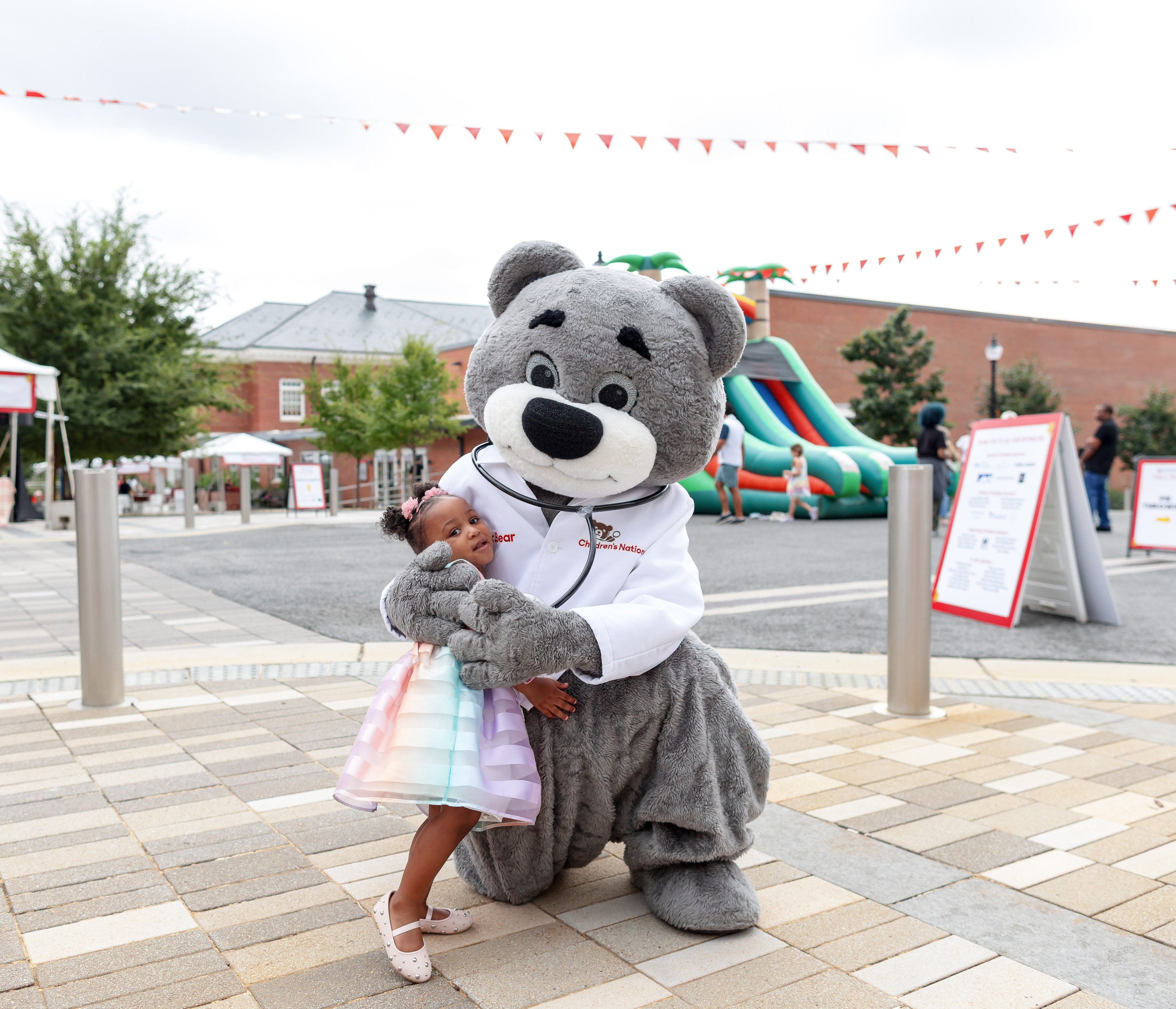 Children's National Hospital mascot, Dr. Bear, and a small child hug at the 2025 Champion's for Children's National Fall fest.