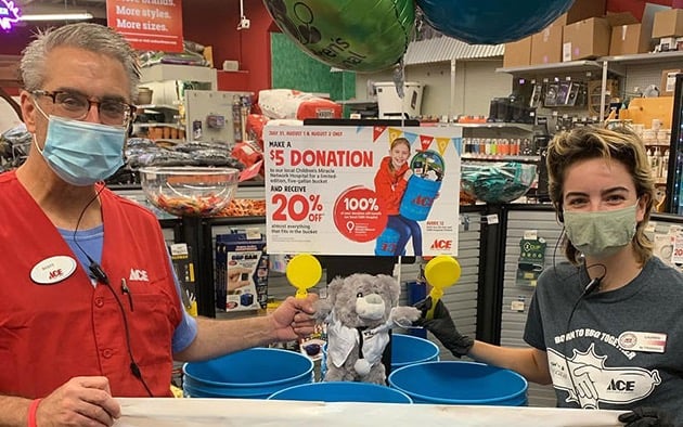 Two Ace Hardware employees pose next to a donation promotion display in a store location.