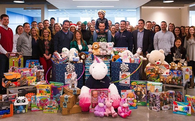 Group photo featuring Atlantic Coast Mortgage staff surrounded by hundreds of toy donations.