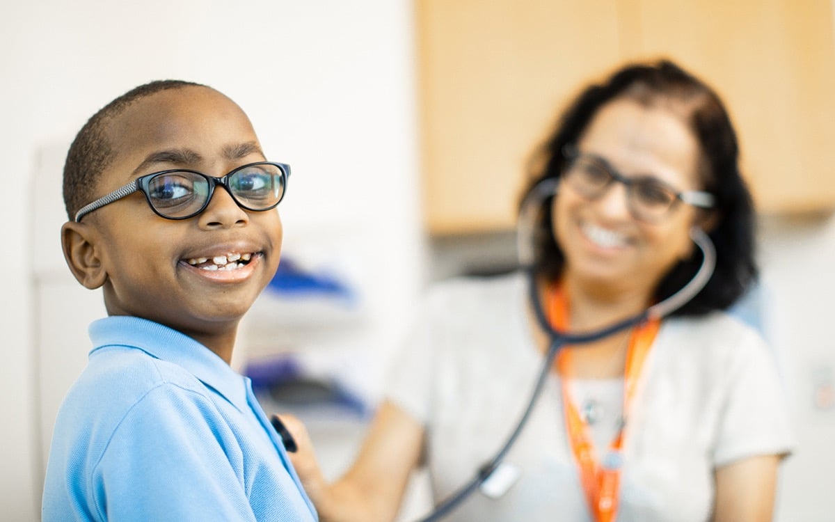 A young patient smiles alongside a doctor wearing a stethoscope.