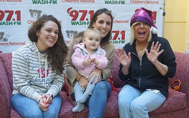 Three women and a baby patient pose for a group photo on a couch during a radiothon event.