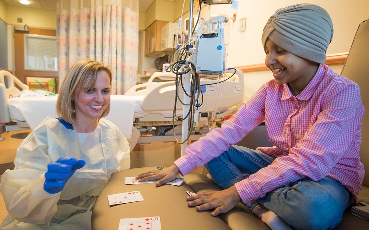An adult volunteer plays cards with a young patient.