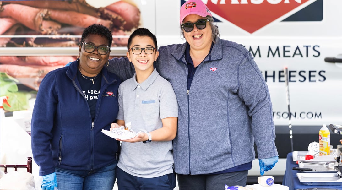 Two female volunteers, one Black and one White, pose for a photo with a teenaged male volunteer.