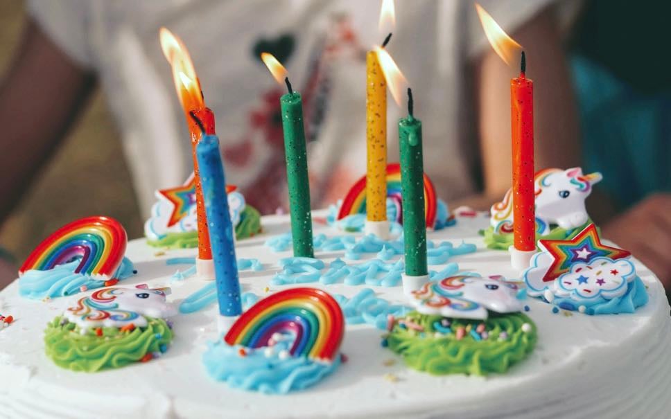 A festive birthday cake decorated with rainbows and lit candles.