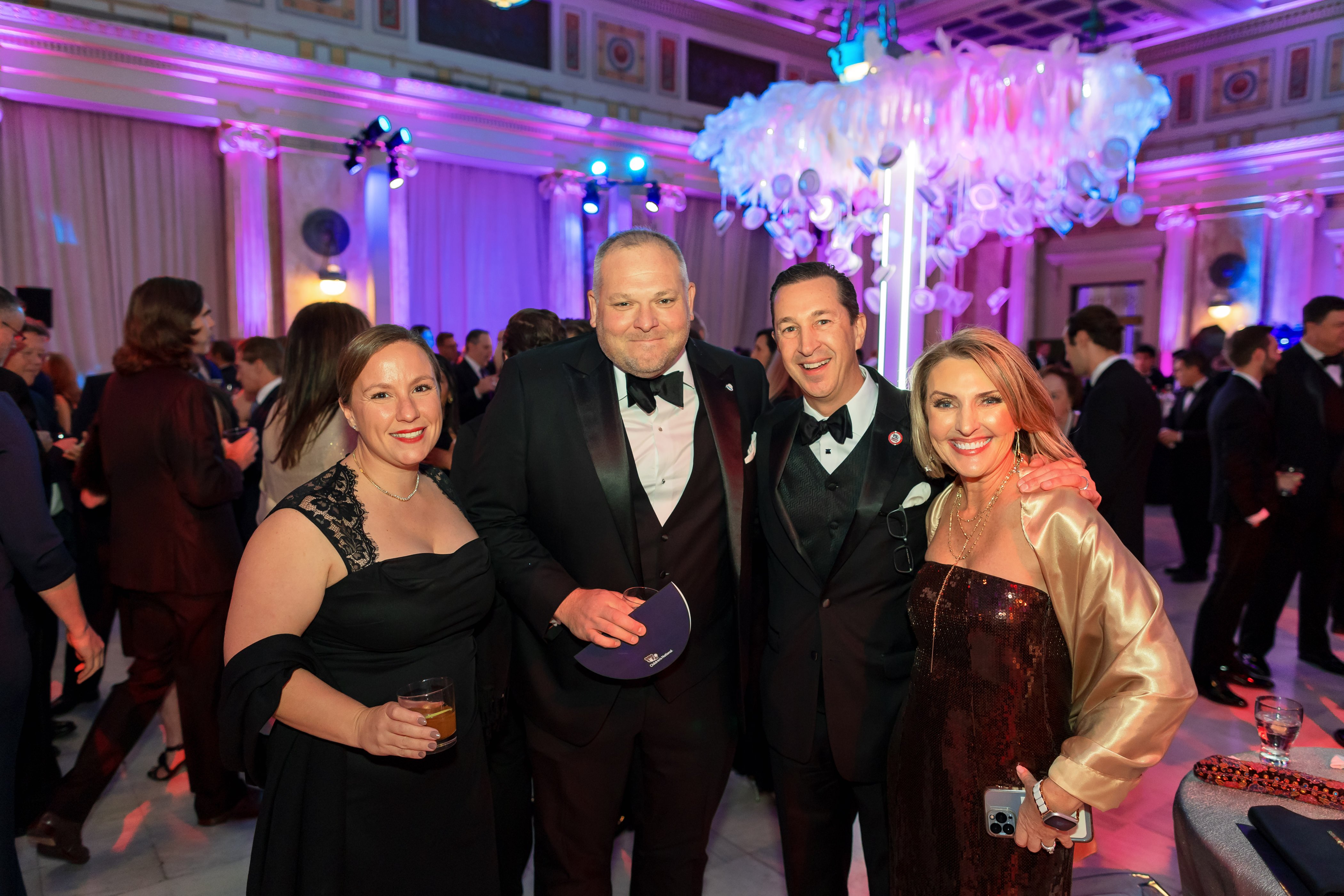 White Hat Gala 2024 attendees smiling while in front of the white hat chandelier