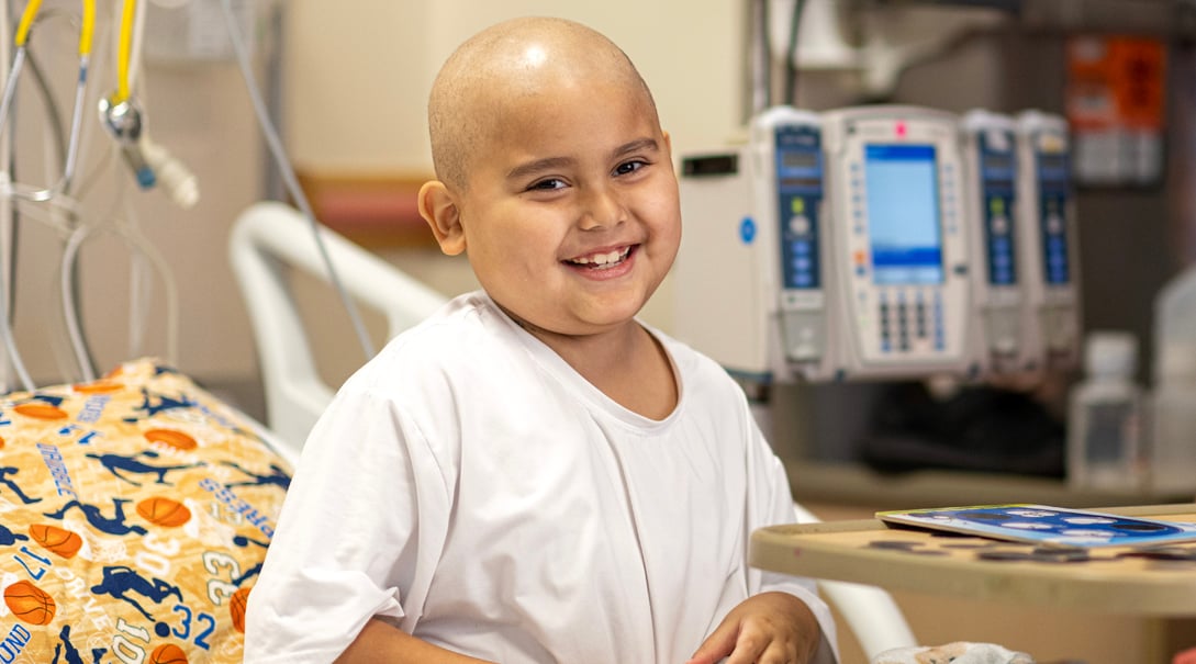A child smiles while wearing a white hospital gown.