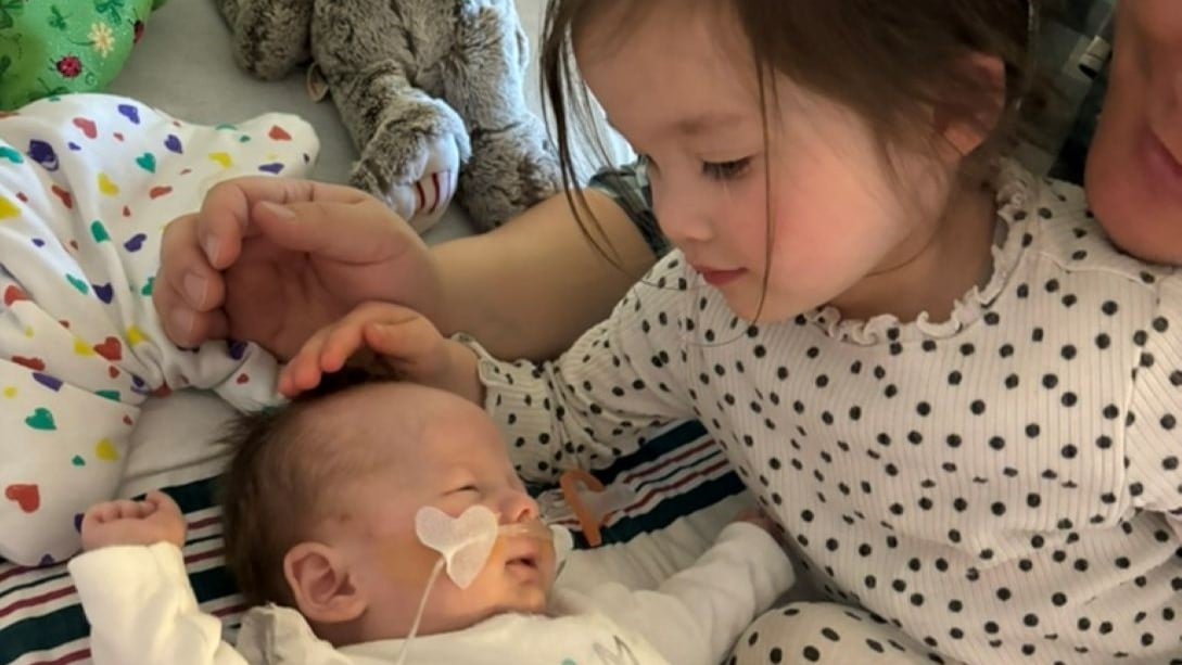 Infant patient, Abby, resting with her big sister and father.
