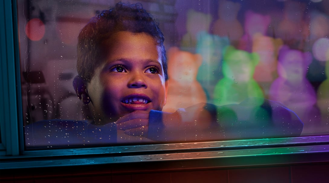 A pre-school aged male patient looks out of the window with wonder as several glowing Dr. Bear figures illuminate the room behind him.