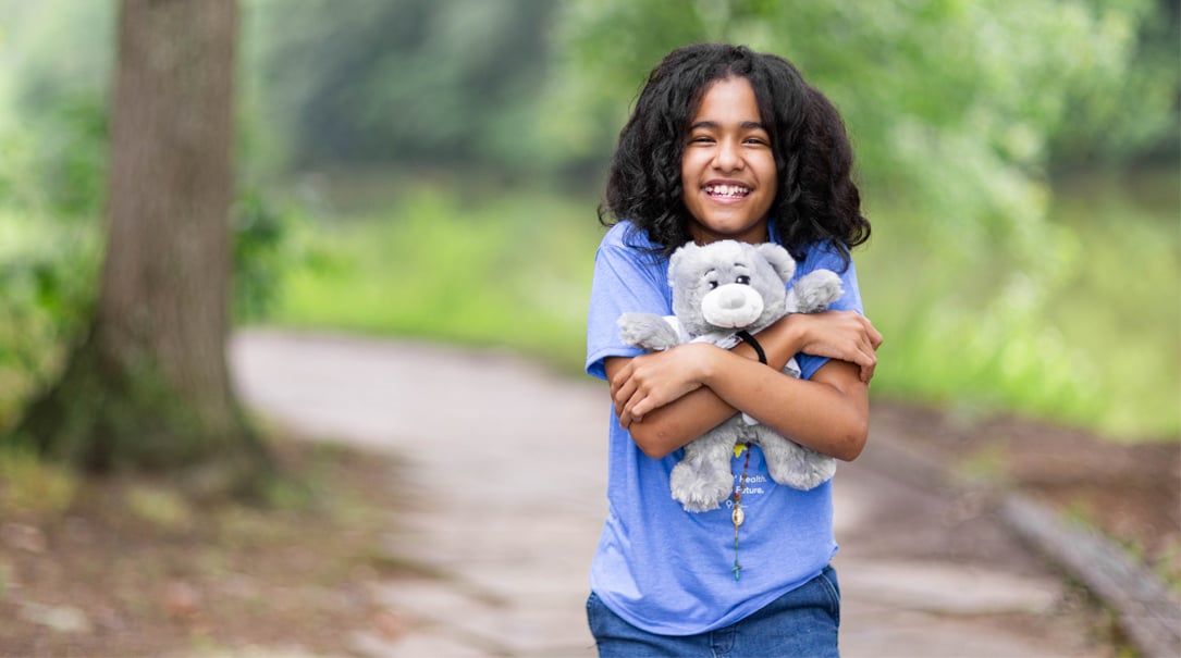 Child smiling at camera while hugging a Dr. Bear plush animal