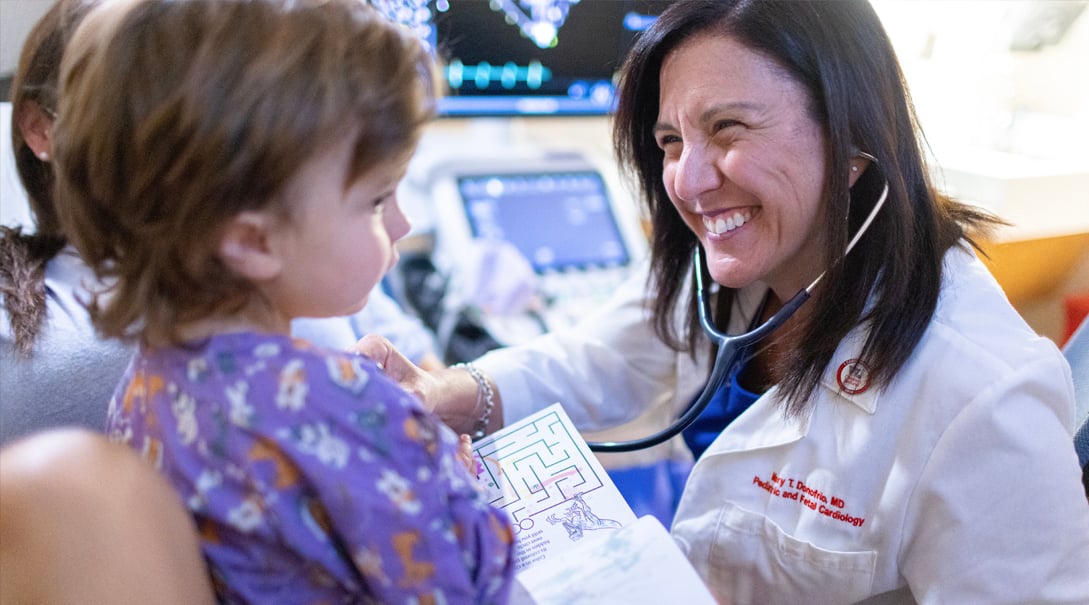 Dr. Mary T. Donofrio, a White female doctor, attends to a White toddler who is a pediatric and fetal cardiology patient.