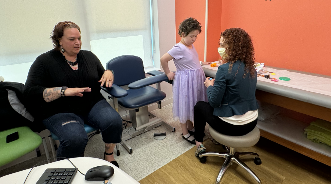 Charlotte, a young female patient, is examined by her doctor, Christina Wiedl, DO, while Charlotte's mother, Jamie, sits nearby