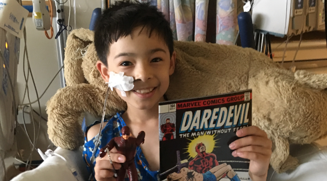 Ethan Low, a young male patient, holds a comic book while cuddling with a big dog plush doll