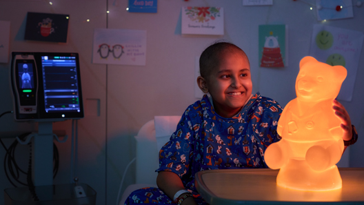 An elementary school aged male patient smiles in the glow of a Light Up Dr. Bear