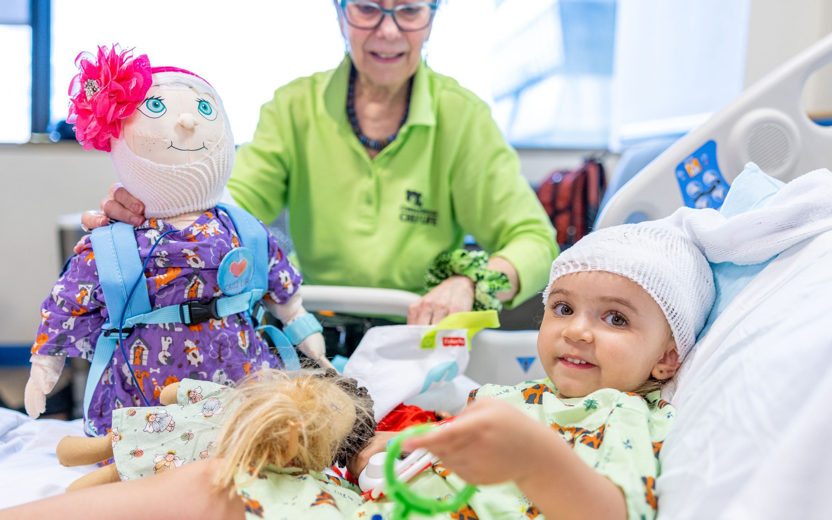 A young cancer and blood disorders patient is attended to by a health professional holding a doll.