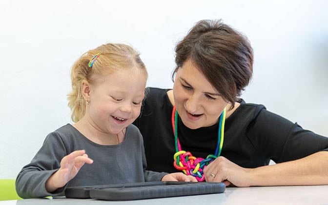 A pre-school aged patient works with an adult and a laptop.