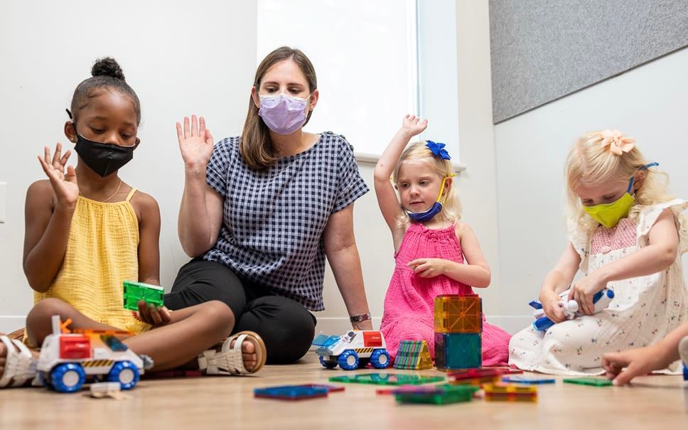 A behavioral health professional at Children's National lead three early-childhood aged girls, one Black and two White, in a therapeutic activity.