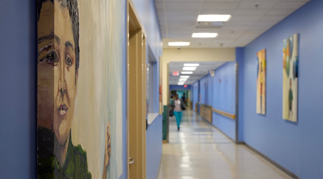 Long view of hospital corridor featuring paintings hanging on blue walls