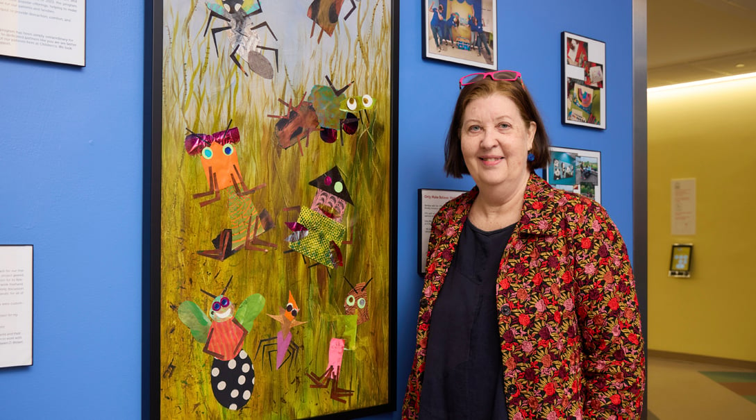 Adult female artist standing in front of a collage painting of insects in grass