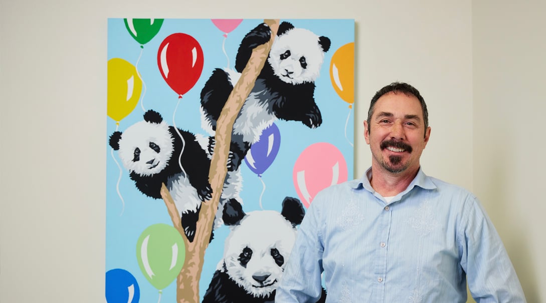 Adult male artist standing next to colorful painting of balloons and panda bears
