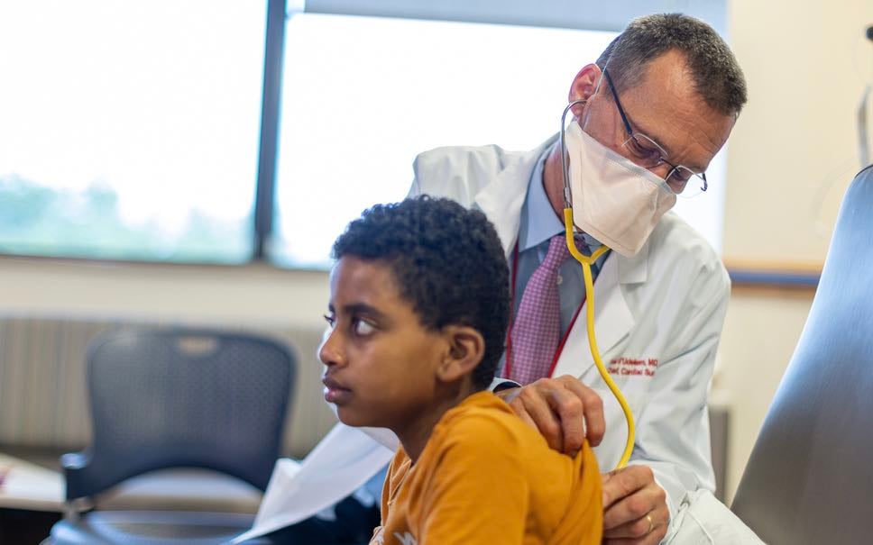 Children's National's Chief of Cardiac Surgery listens to the heartbeat of an elementary school aged Black male patient.
