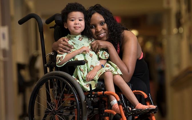 An early grades aged patient in a wheelchair poses with their mother.