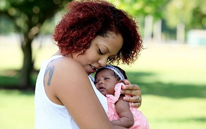 A mother cradles her infant outdoors.