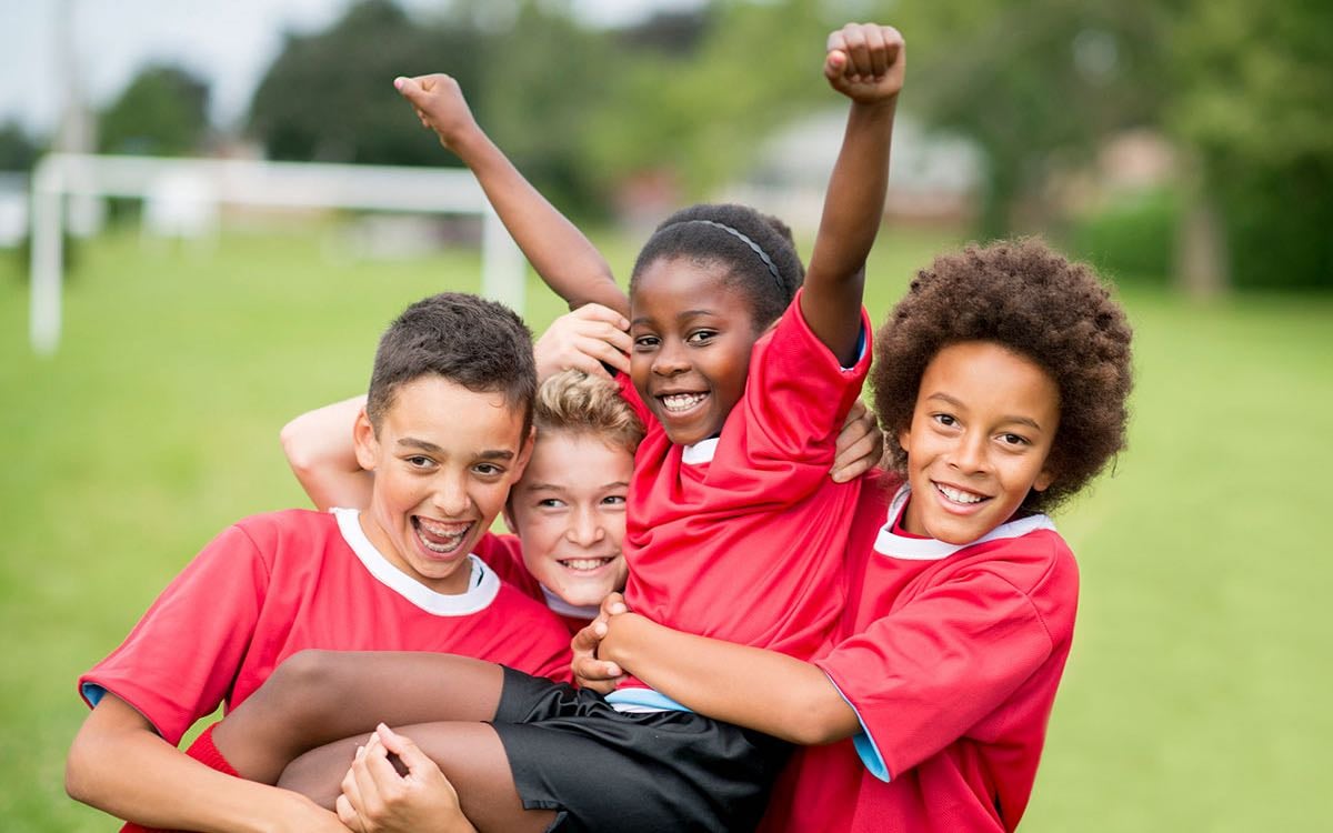 Three elementary school aged children hold up a fourth child in victory.