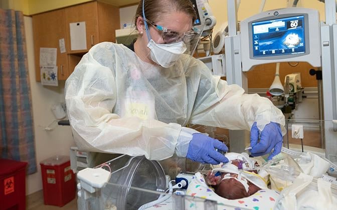 A neonatal professional attending to a newborn patient in an incubator.