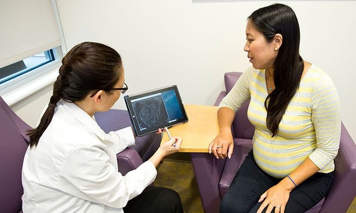A female Asian doctor shows a female Asian expectant mother a digital image of her scan.