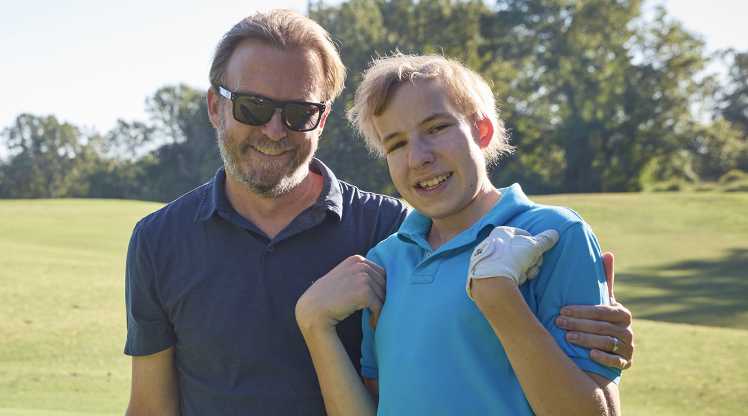 A White father and son pose together at a Children's National fundraiser on a golf course.