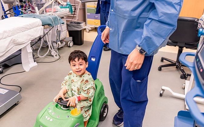 A toddler aged patient rides in a toy car.