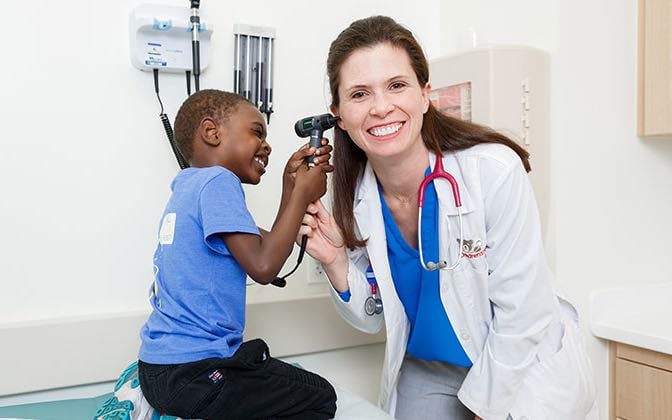 A young Black male patient looks into his White female doctor's ear with her otoscope. 