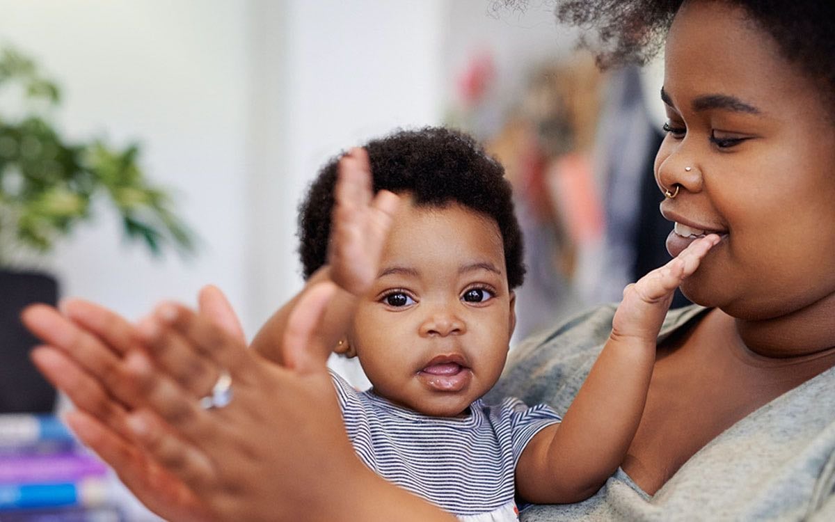 An infant and their mother clap their hands.T