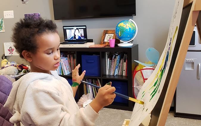 A pre-school aged mixed race female cancer patient paints at an easel during an art therapy session.