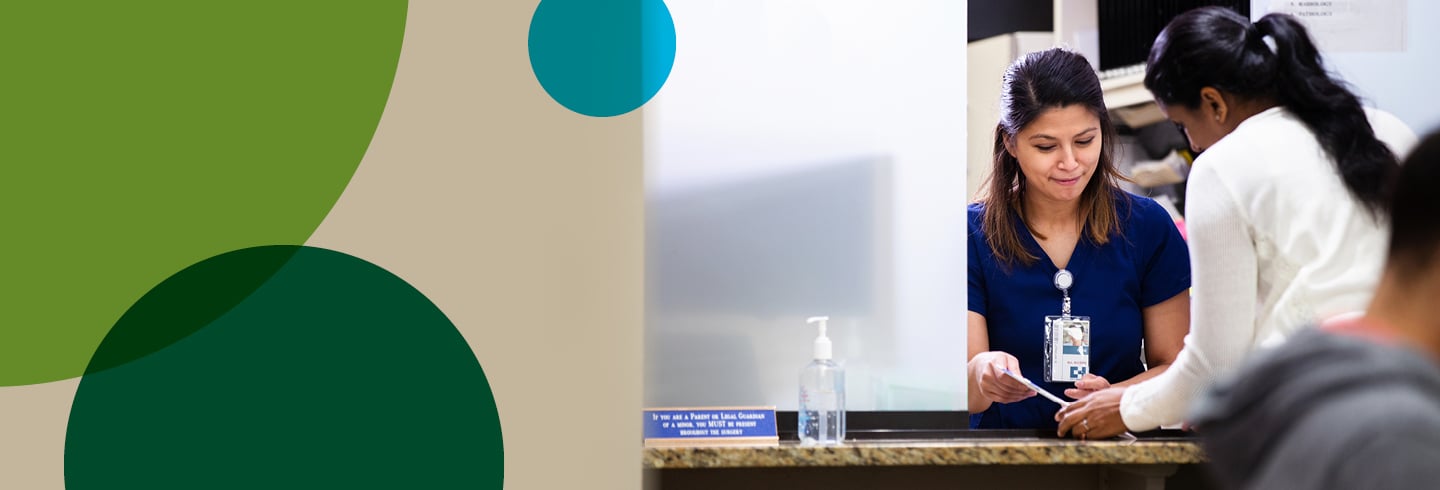 Female patient talking with hospital staff at the front desk.