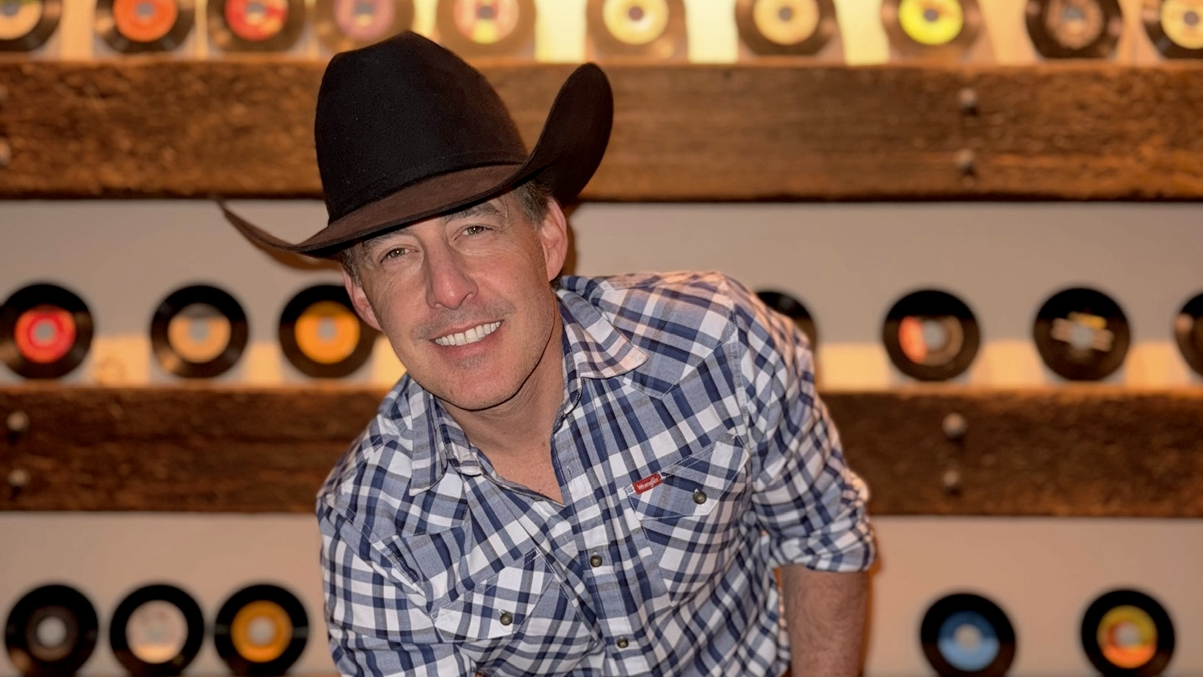 Aaron Watson headshot with wooden shelves of 45 records in the background.