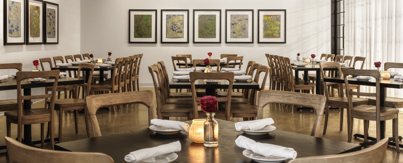 Katie's Pizza & Pasta Osteria dining room with wooden tables and chairs set with plates, utensils, candles, and single rose in vase.