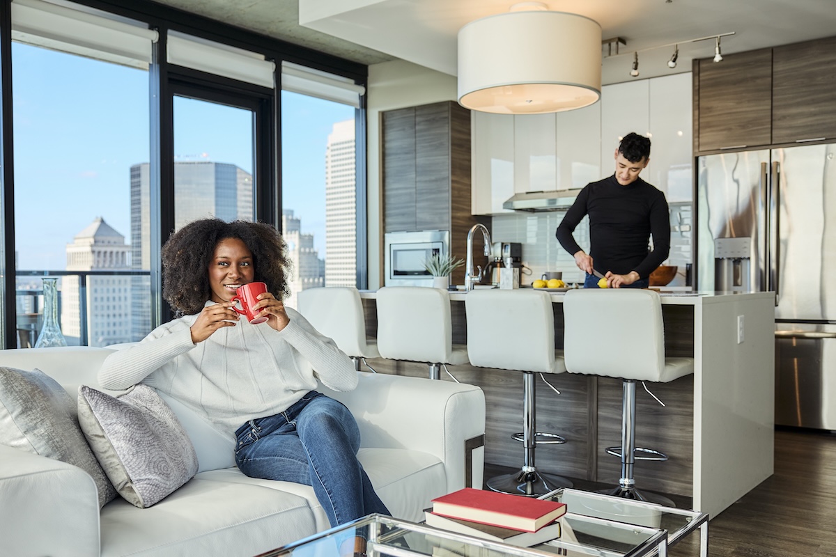 Couple in a modern apartment kitchen and living area with floor to ceiling windows at One Cardinal Way