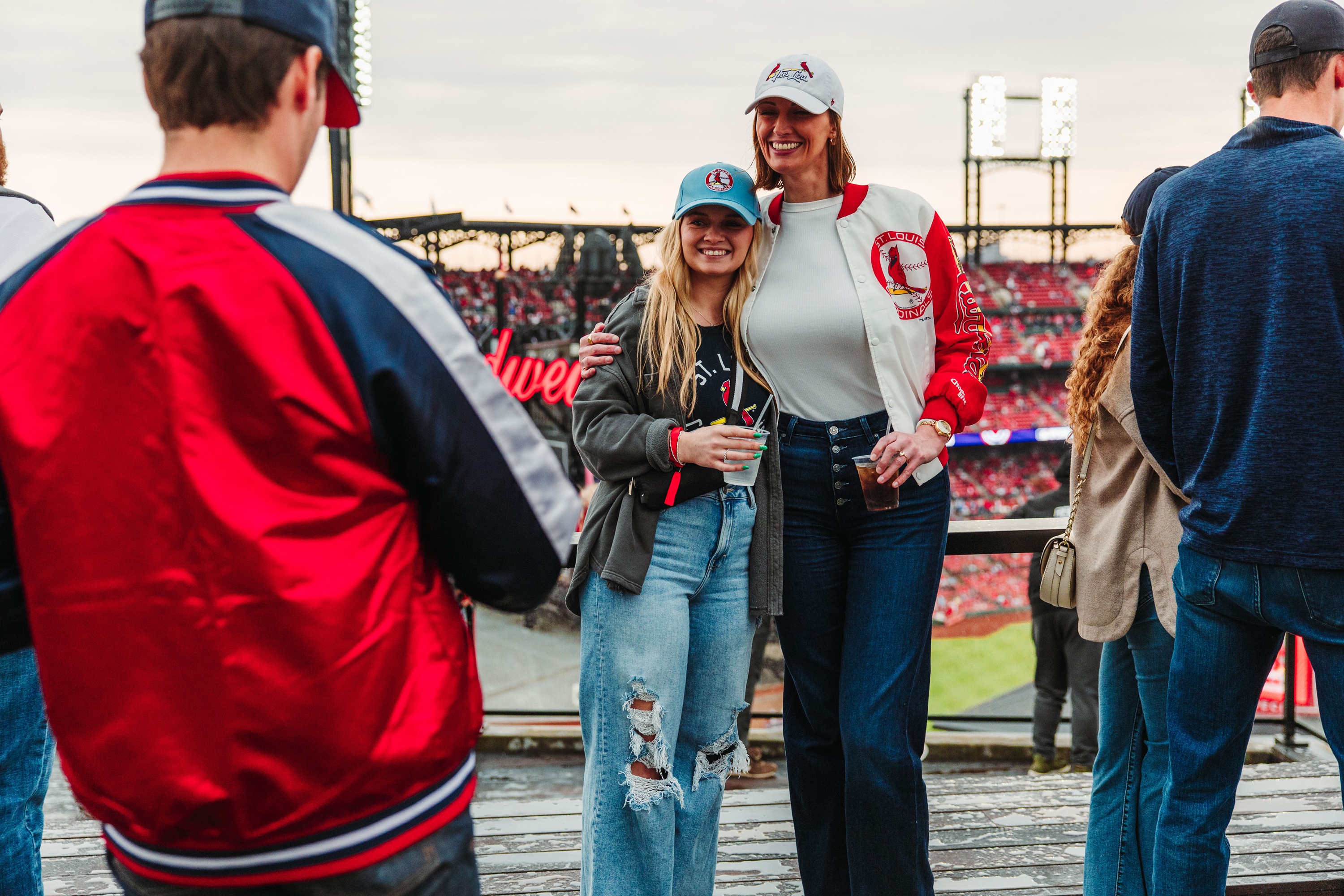 two women taking a picture at a rooftop with a stadium in the background