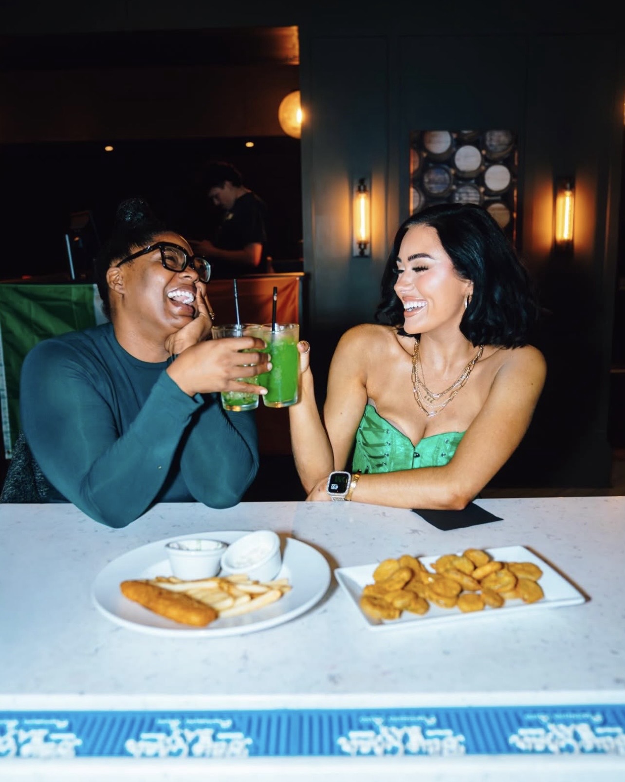An image of two women cheersing their drinks at the bar.