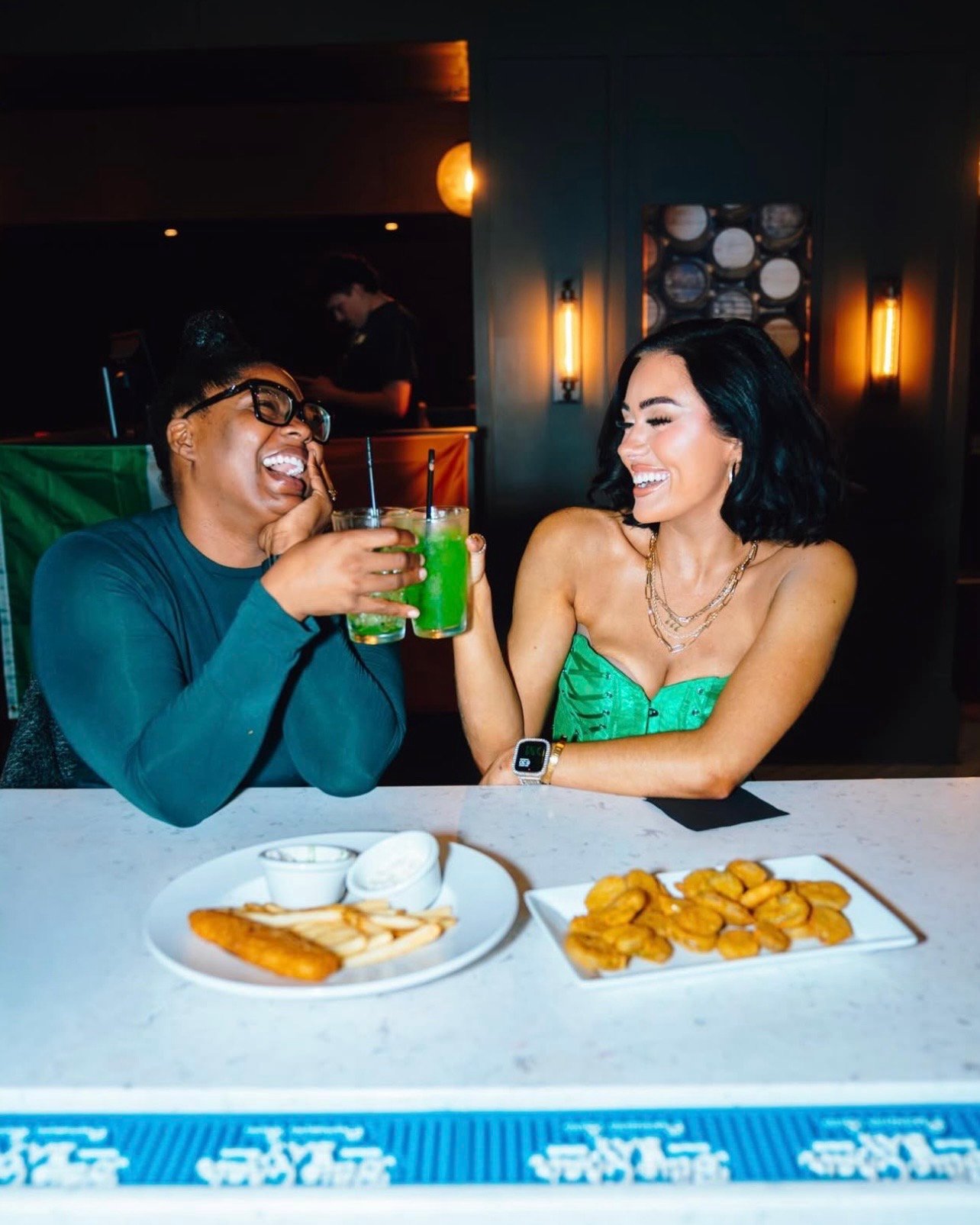 An image of two women cheersing their drinks at the bar.