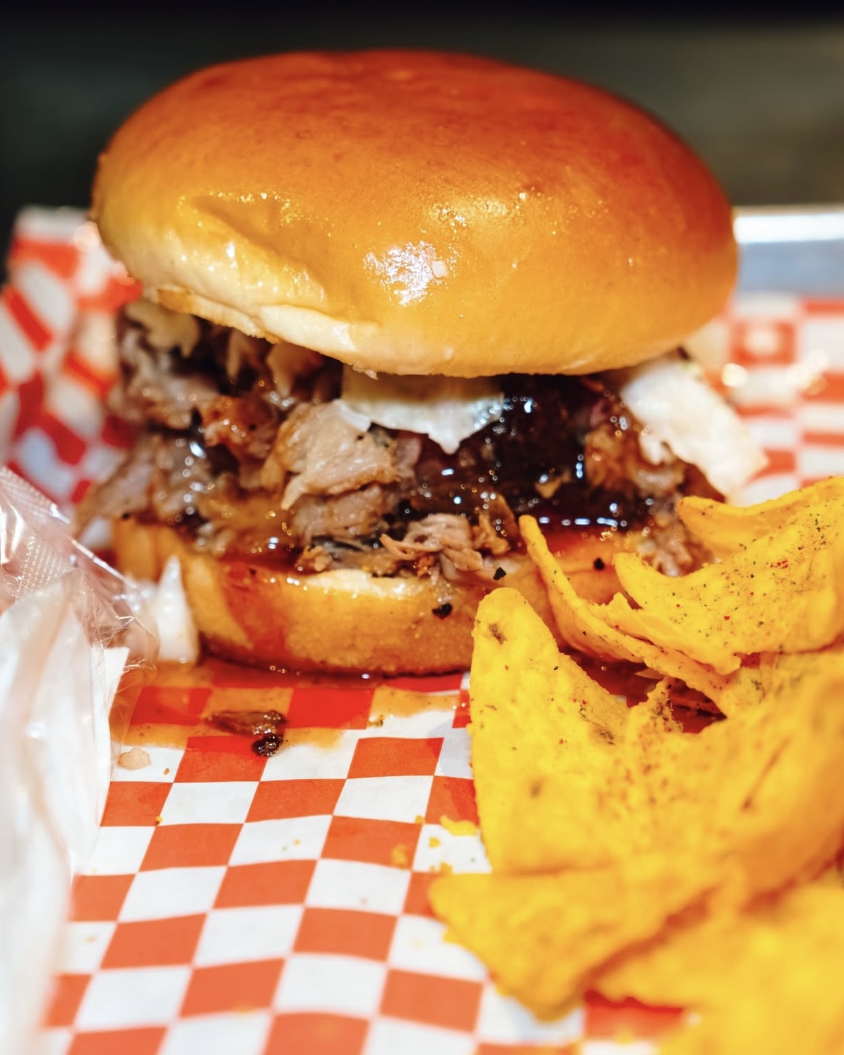 An image of a pulled pork sandwich and chips on a tray.
