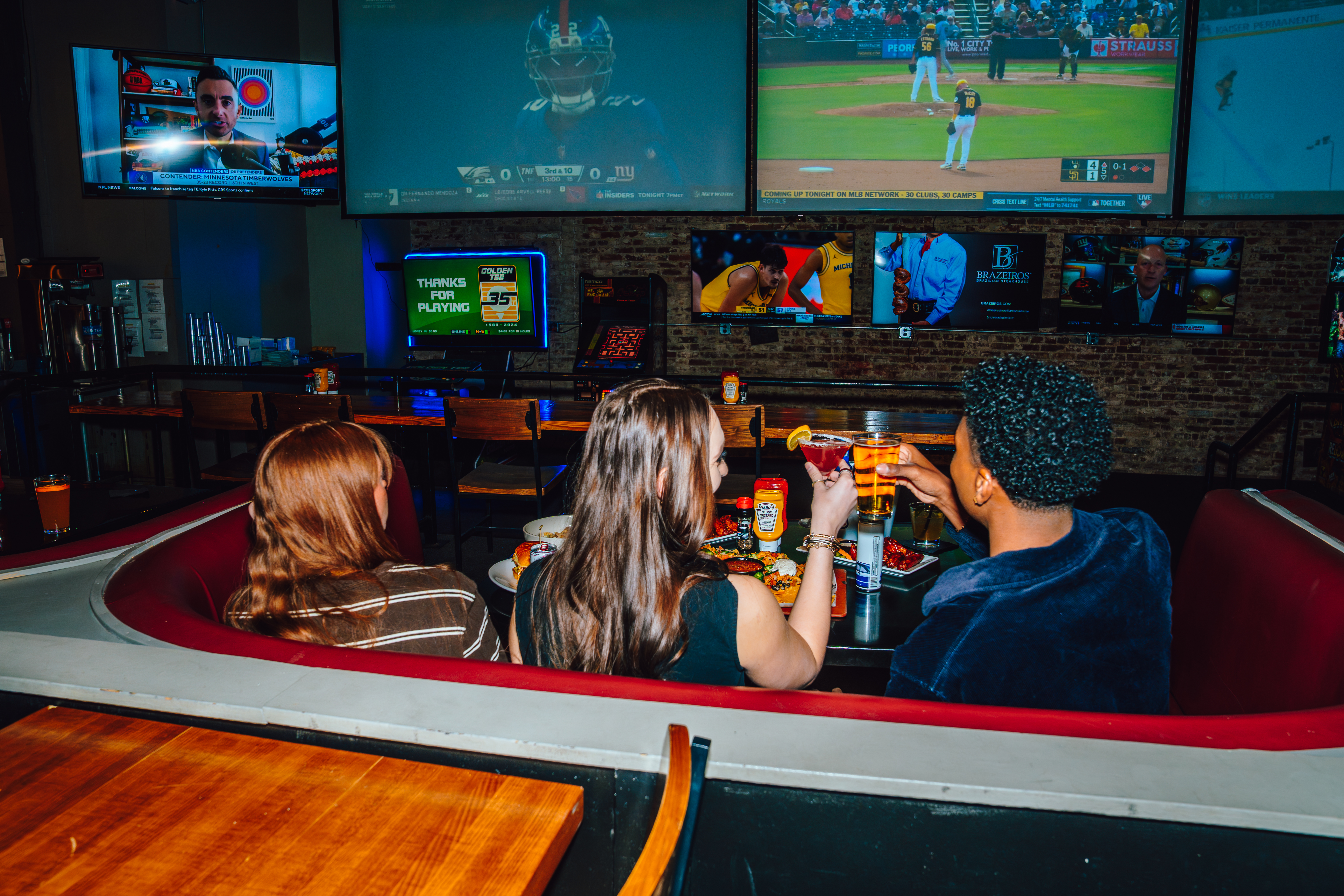 An image of 3 people watching sports on the big screens at Sports and Social.